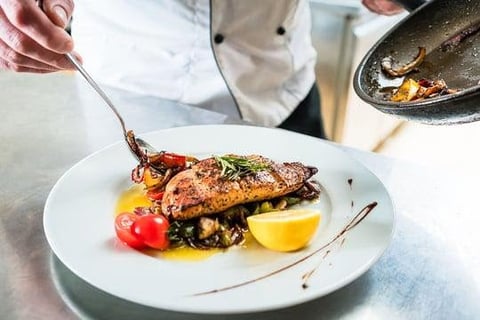 Chef plating an elegantly seared fish fillet with garnish and sauce on a white plate