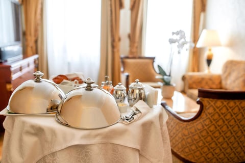 Room service tray with silver domed covers and condiments on a table in an upscale hotel bedroom